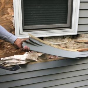 hand prying off rotted siding under window
